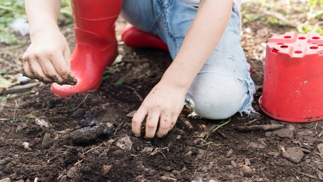 Cropped view of child in jeans and red boots playing in dirt (selective focus)
