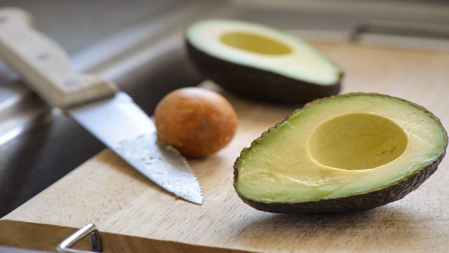 Avocado cut in half on a cutting board over a sink with knife in pit