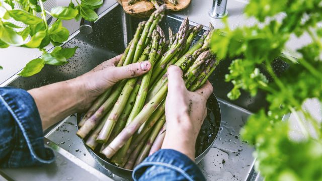 cropped shot of male hands in soil washing fresh asparagus in kitchen sink